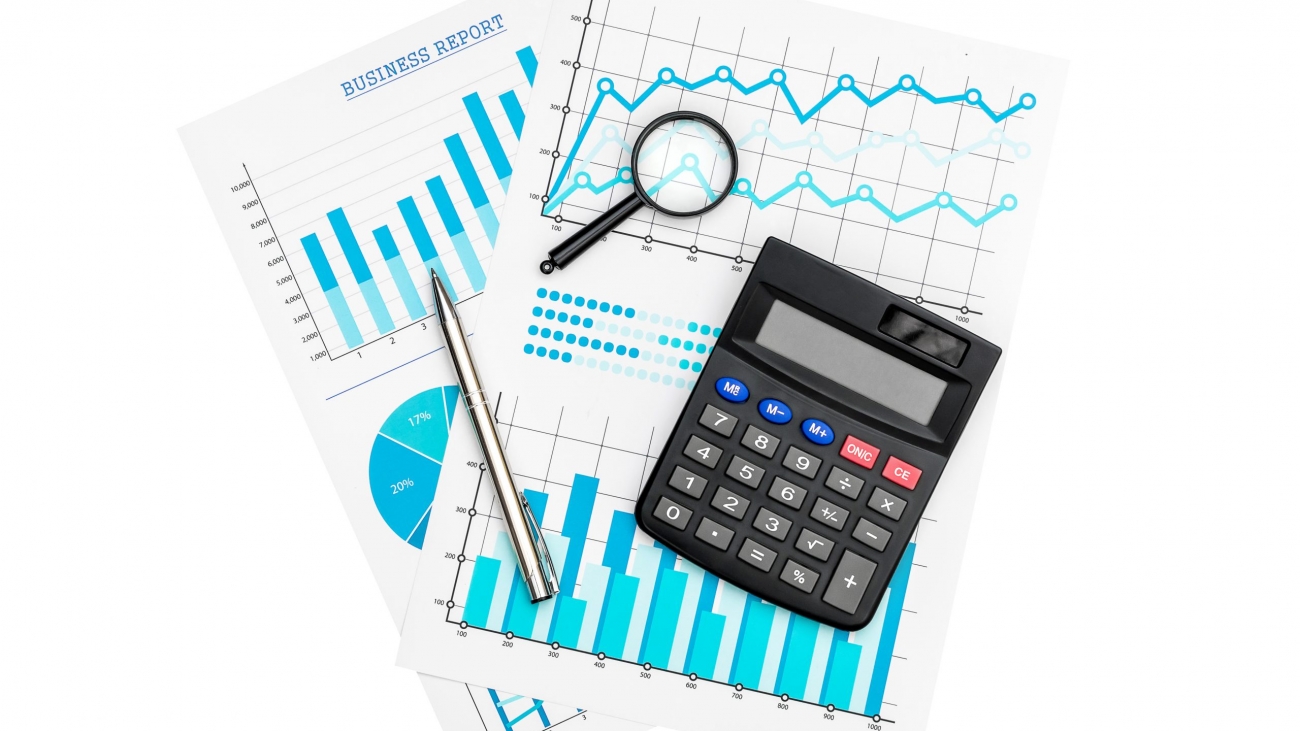 Paper financial graphs and charts with calculator, magnifying glass and pen isolated on white.